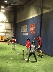 Coach with young baseball players practicing hitting<br />
